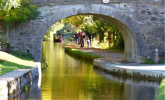 Scene of one of Llangollen canal's historic stone bridges (46) With a view of canal walkers and one of Llangollen Wharf's horse drawn boats in the dis